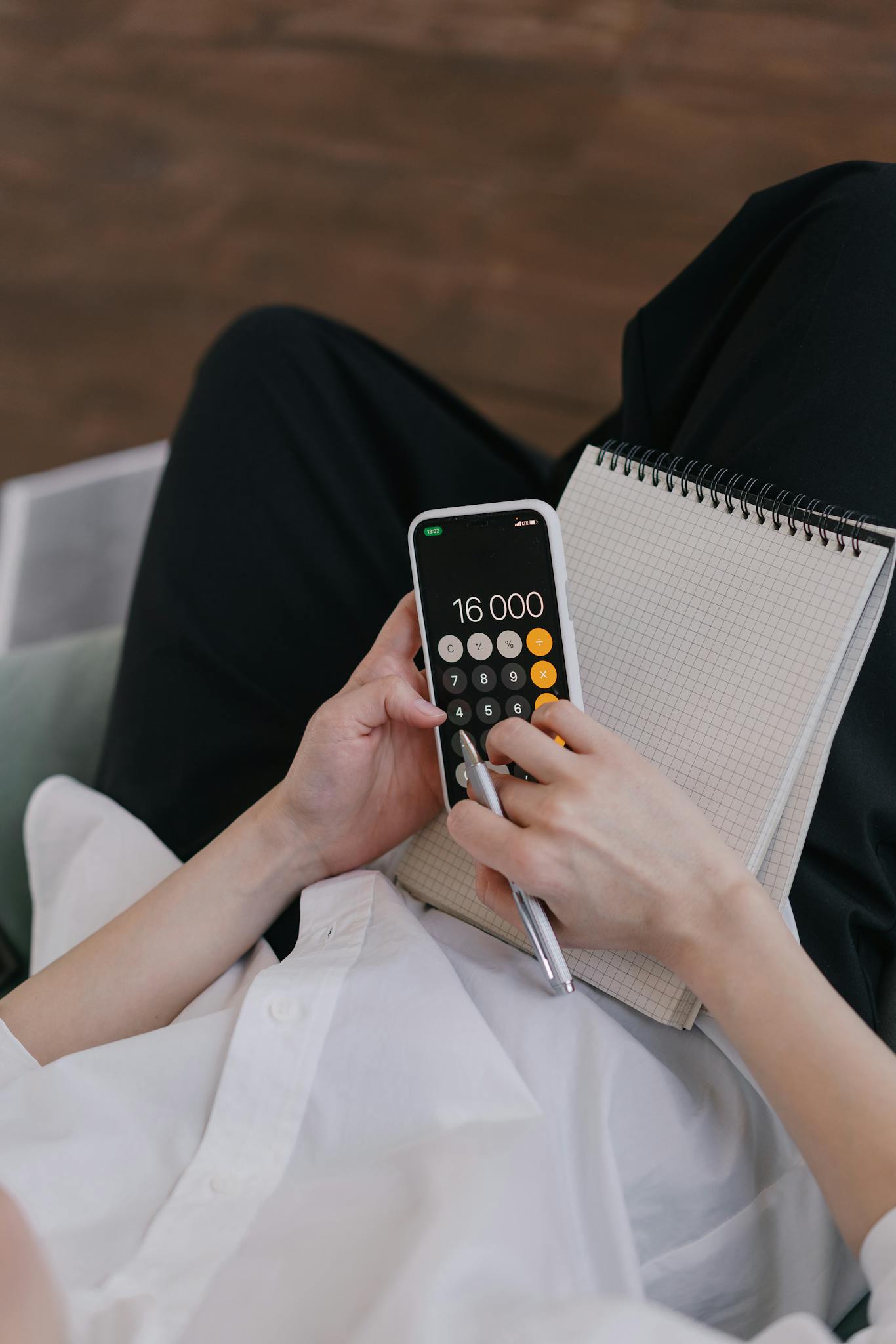 Close-up of a person using a smartphone calculator while planning finances with a notebook.