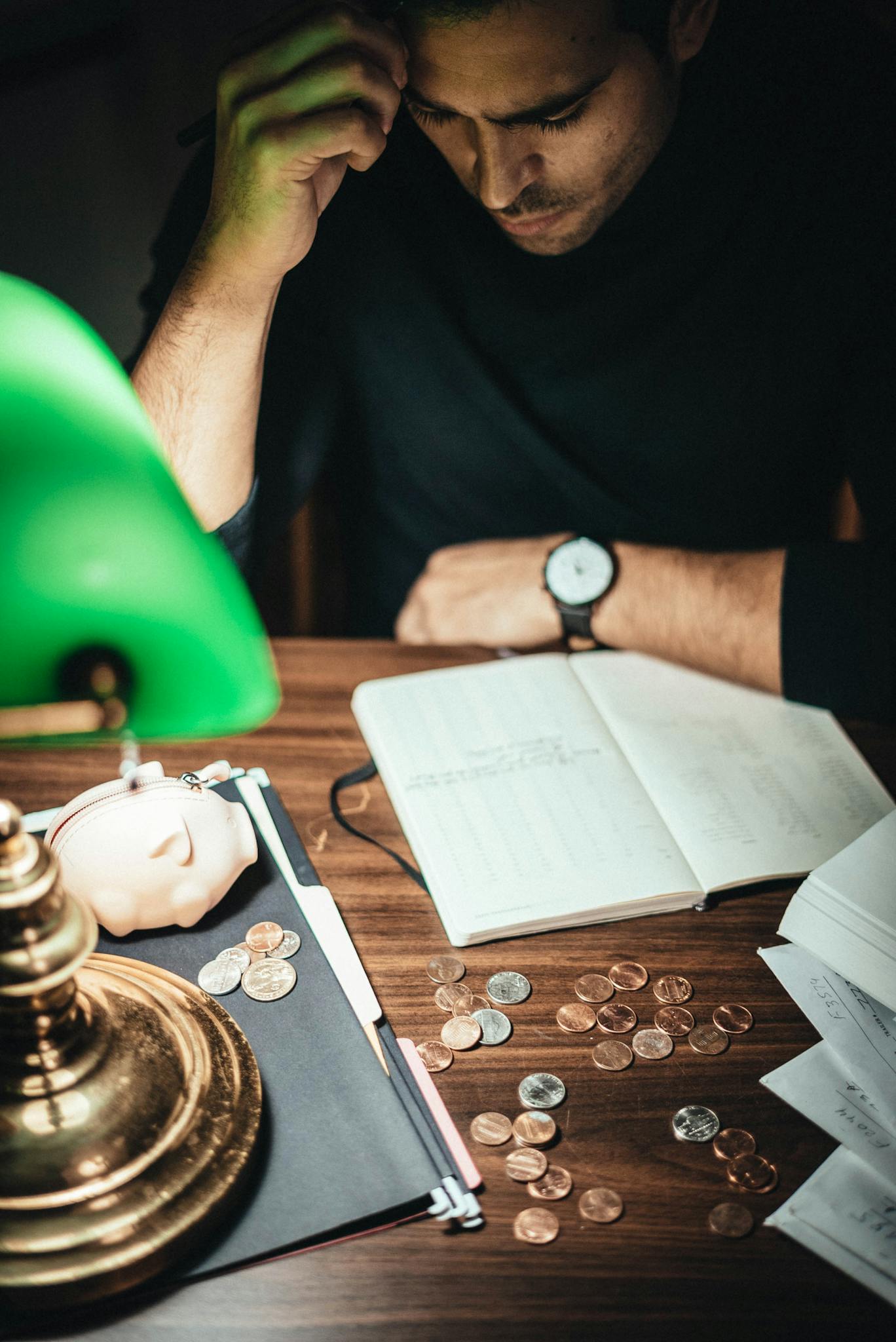 High angle of concentrated man at table with retro lamp and coins contemplating on notes in journal