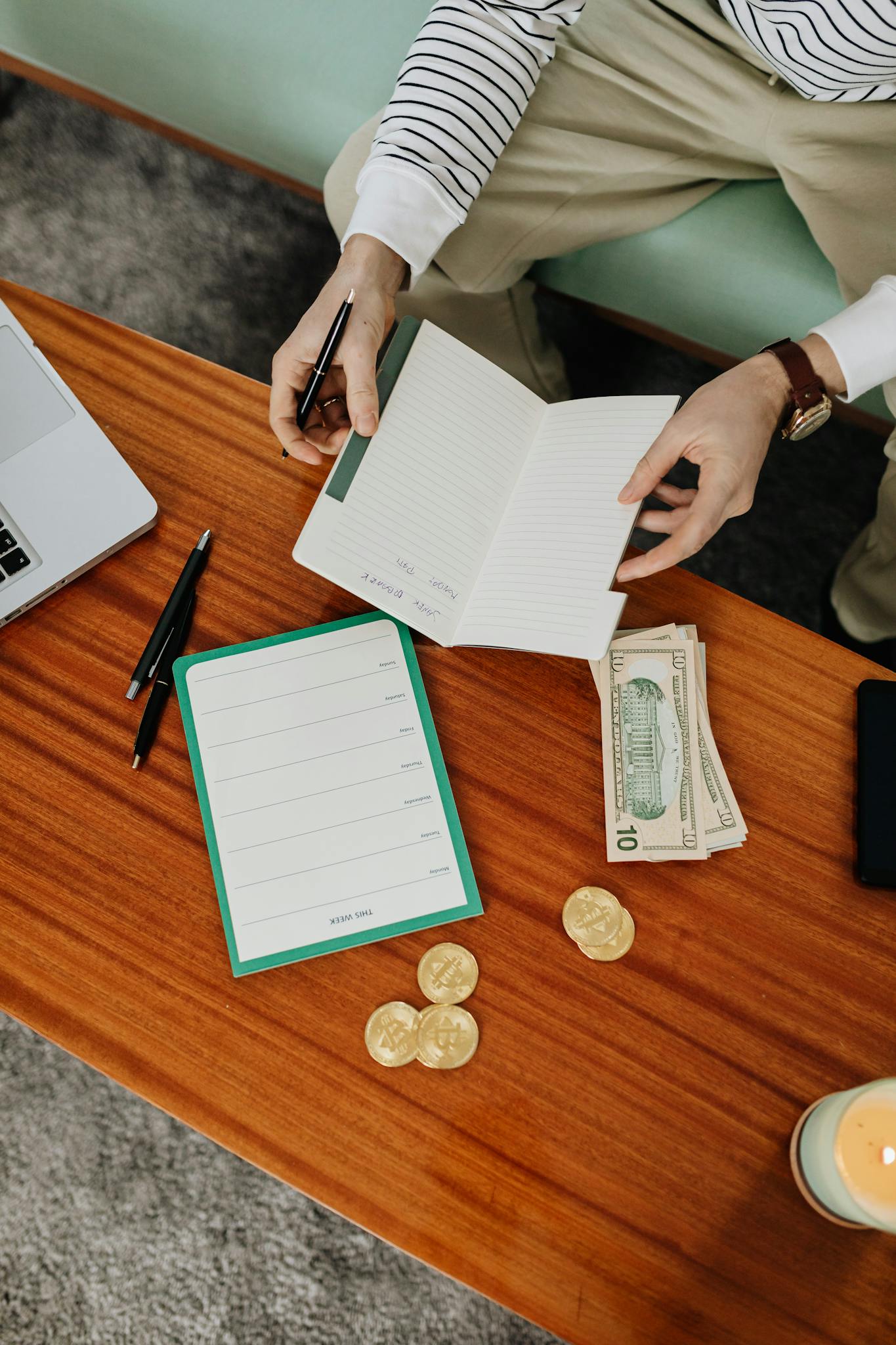 Person organizing budget with notebook and cash on a wooden table, perfect financial planning concept.
